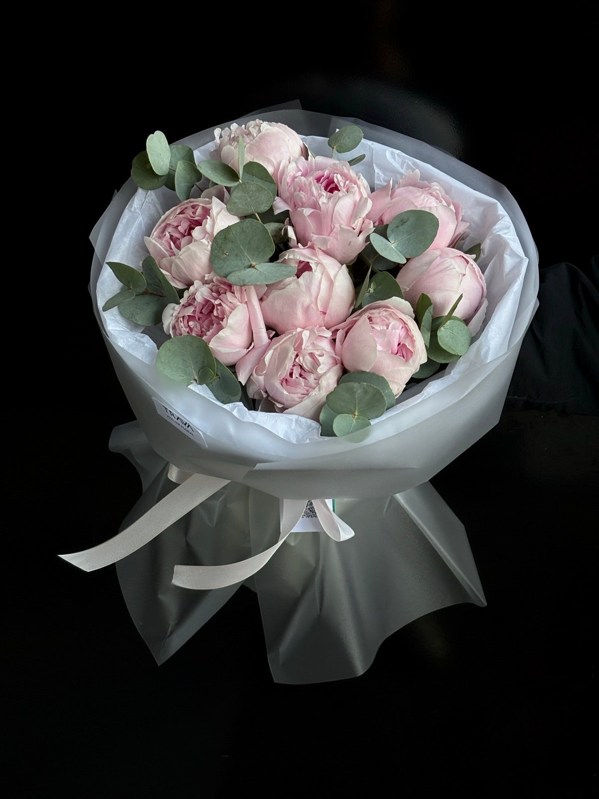 Buchet de bujori roz cu eucalipt, ambalat elegant în hârtie albă semi-transparentă și panglică satinată, TRAVA Atelier Floral Oradea. Livrare gratuita la domiciliu.