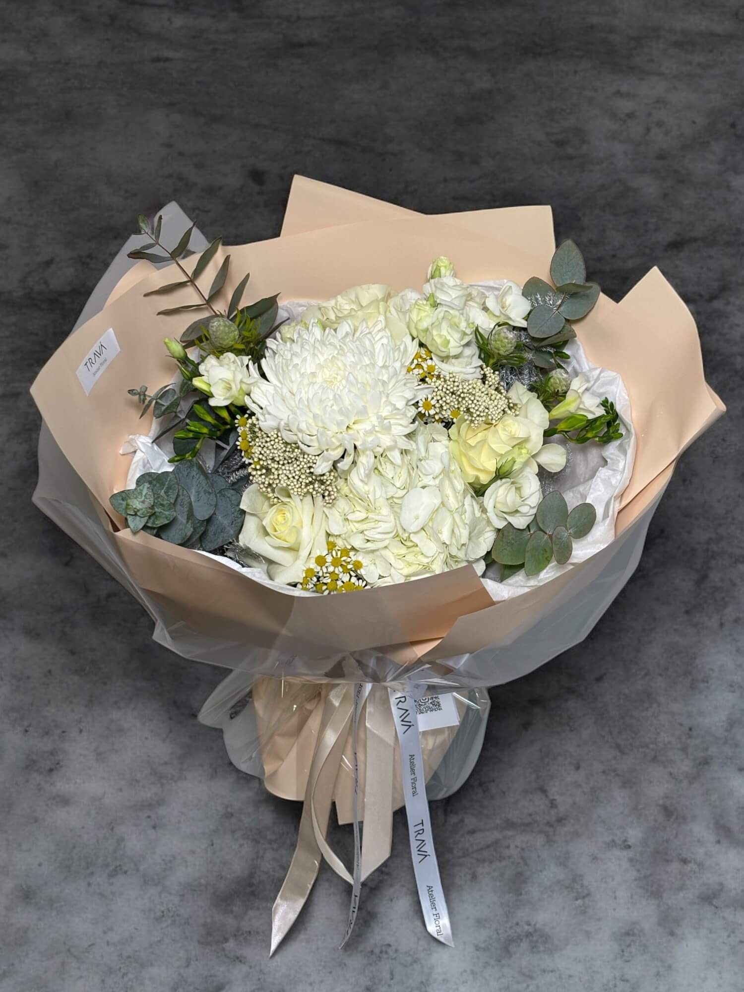 Buchet de flori care contine crizantema alba, hortensie alba, trandafiri albi, lisianthus alb, musetel, ozothamnus, eucalipt, in ambalaj semi transparent cu panglica de satin si hrana pentru flori