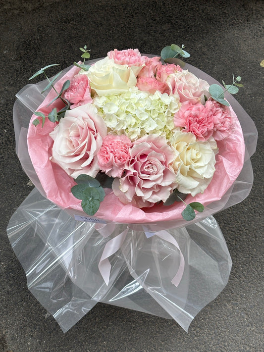 Buchet pastel cu trandafiri roz și albi, hortensie albă, garoafe roz și eucalipt, împachetat elegant cu hârtie roz și fundiță satinată.