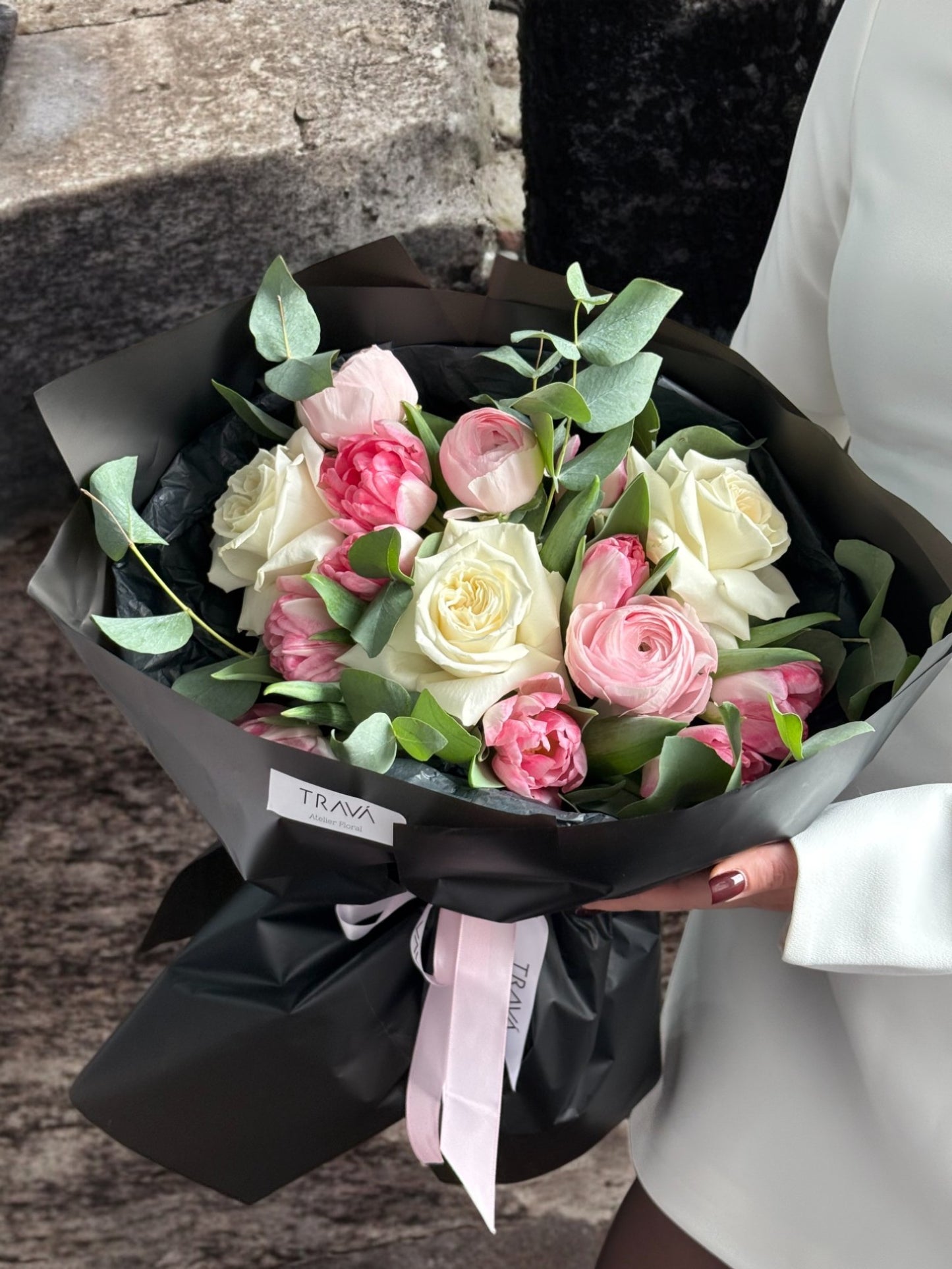 Buchet de flori cu trandafiri albi, ranunculus și lalele roz, ambalat elegant în hârtie neagră cu panglică roz - TRAVÁ Atelier Floral