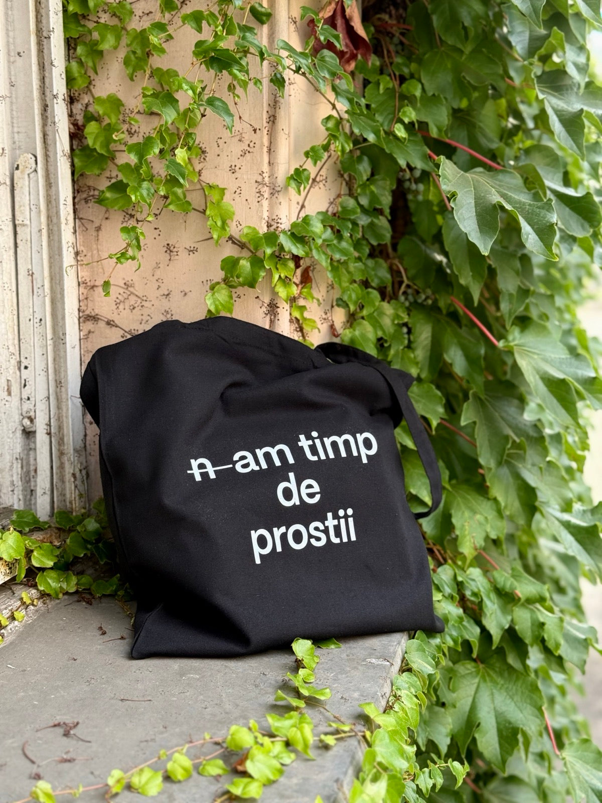 Sacosa din bumbac negru 100%, cu mesaj n-am timp de prostii, surprinsă în decor natural cu iederă.