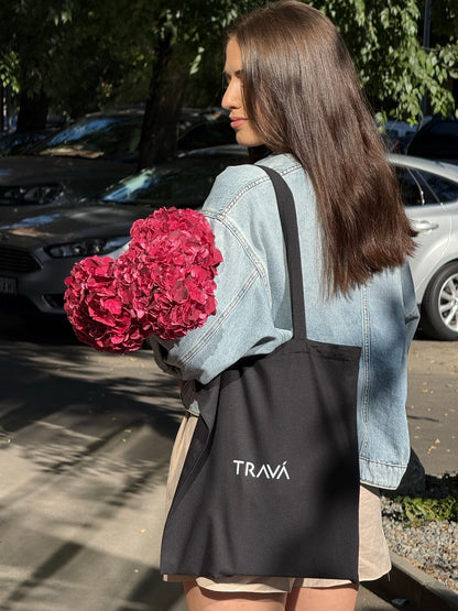 Geantă tote bag TRAVÁ din pânză neagră, purtată pe umăr, cu logo imprimat pe spate.
