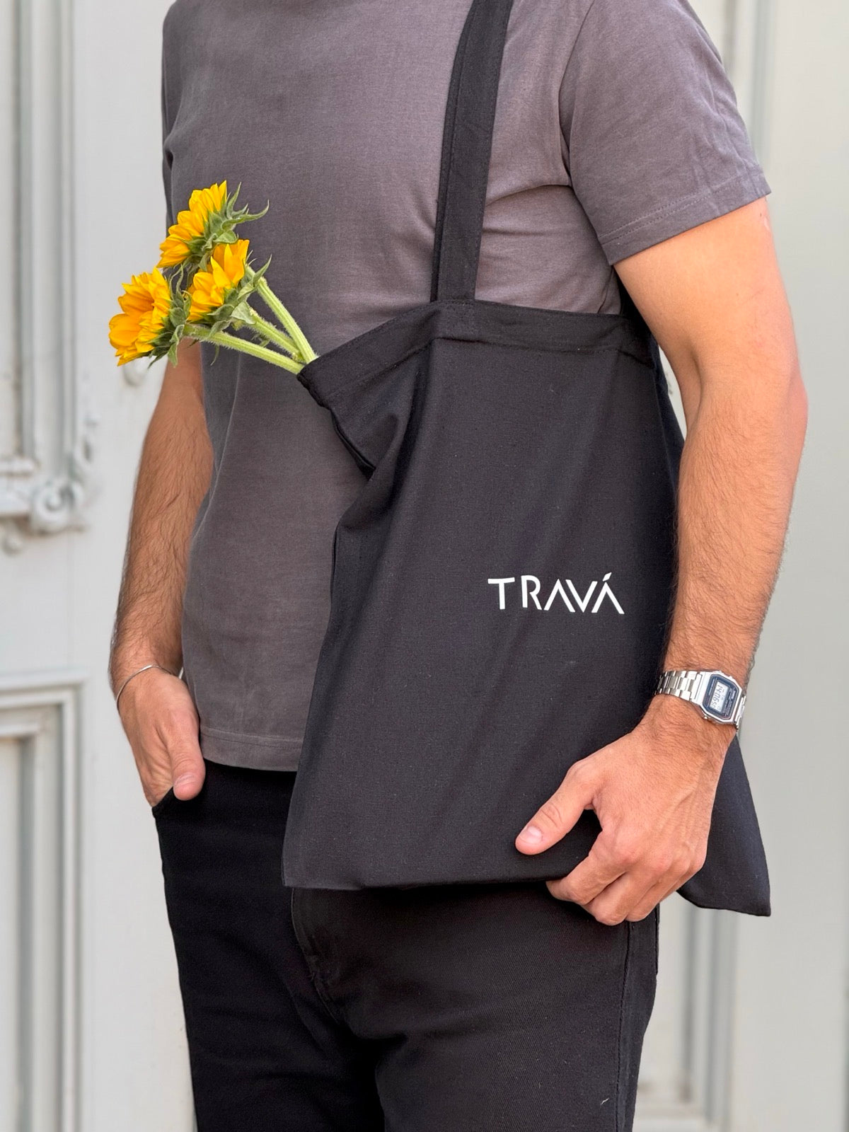 Torba neagră TRAVÁ din bumbac, purtată pe umăr, cu logo alb și flori galbene în interior.