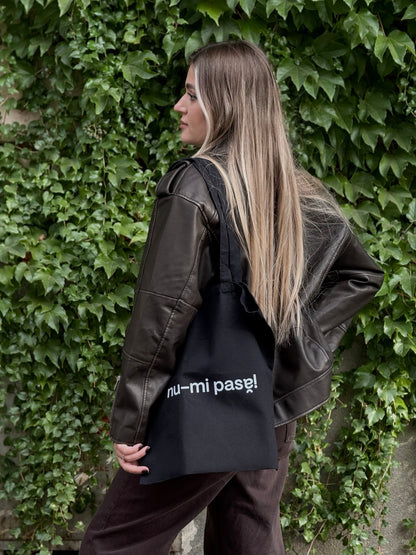 Tote bag din bumbac negru 100%, cu mesaj ironic Nu-mi pasă!, purtată casual pe umăr.