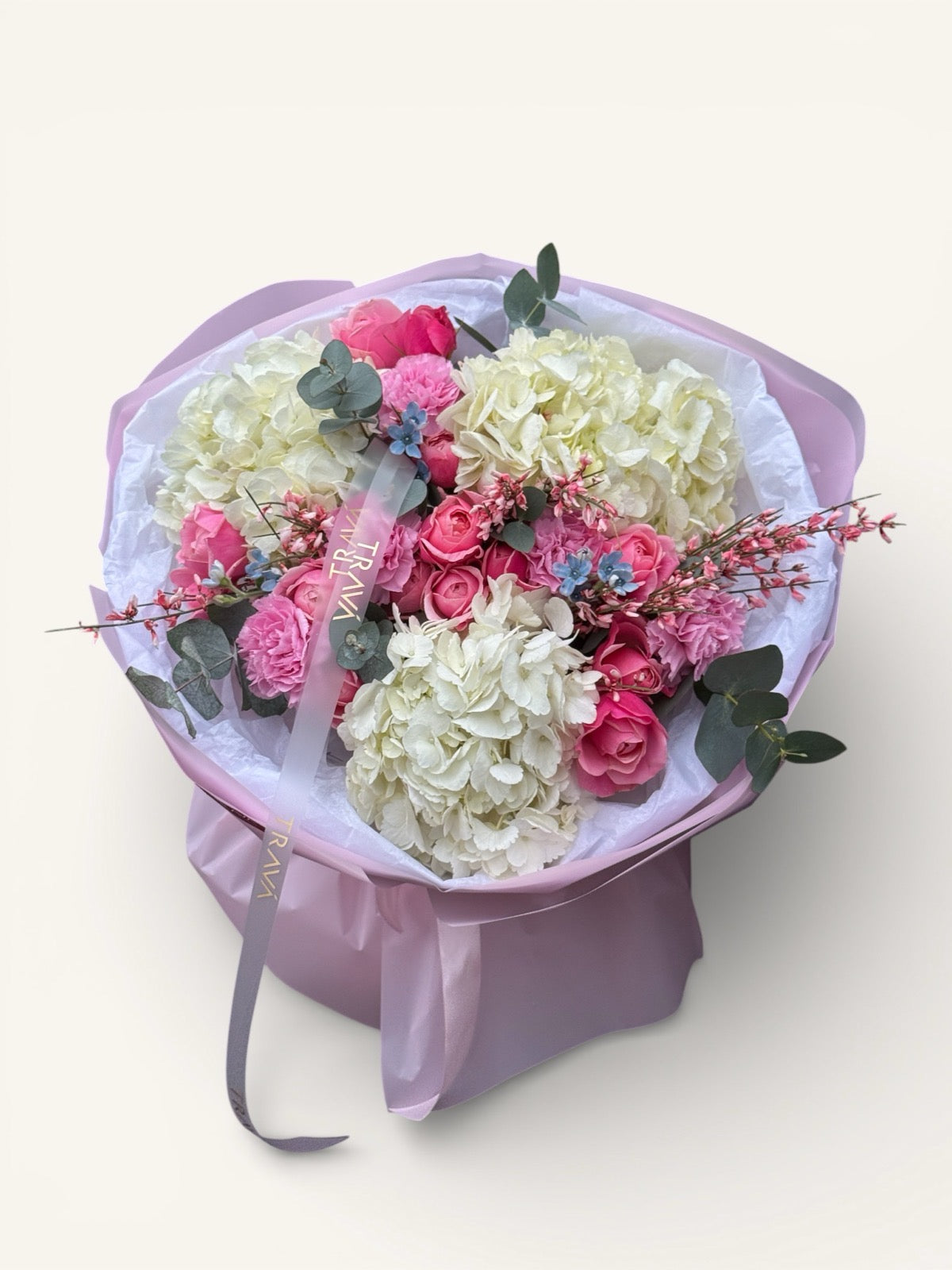 Buchet rotund cu hortensie albă și trandafiri roz în ambalaj de hârtie roz, cu panglica Trava Atelier vizibilă central.