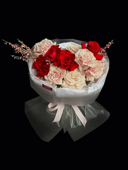Buchet de trandafiri rosii si roz cu fire de genista ambalat in folie mata si legat cu funda roz pal.