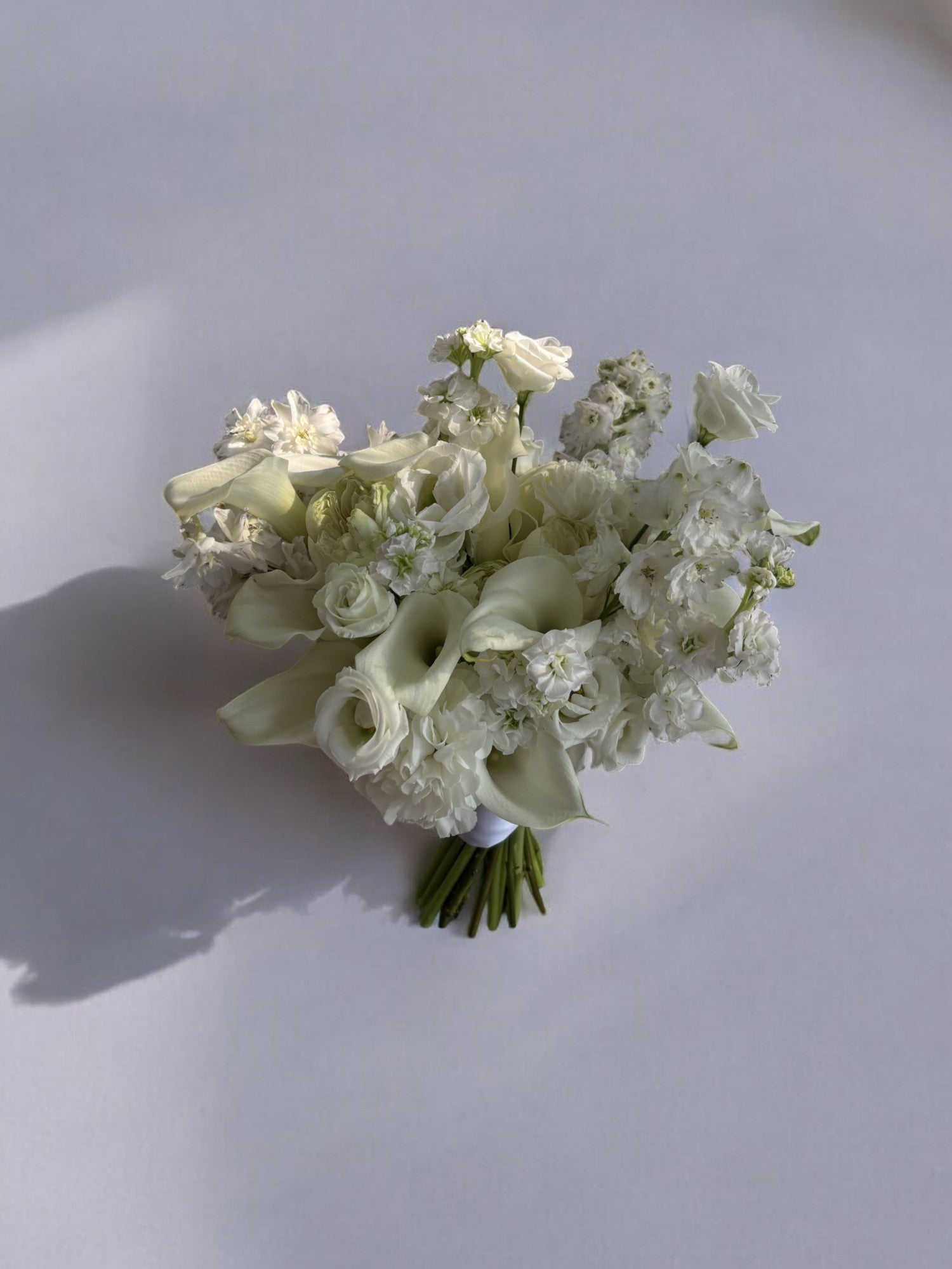 Buchet de mireasă din flori albe, cu cale, delphinium, trandafiri, lisianthus și garoafe, perfect pentru nunți și ocazii speciale.