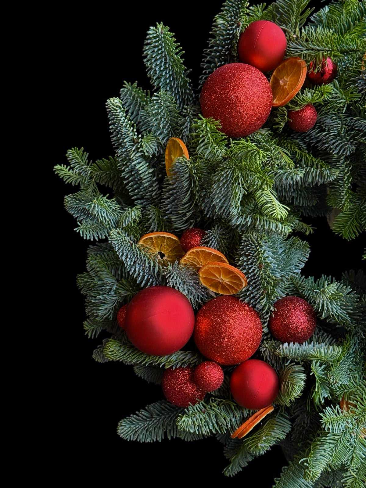 Detaliu coroniță de Crăciun cu conifere, globuri roșii și portocale deshidratate de la TRAVA